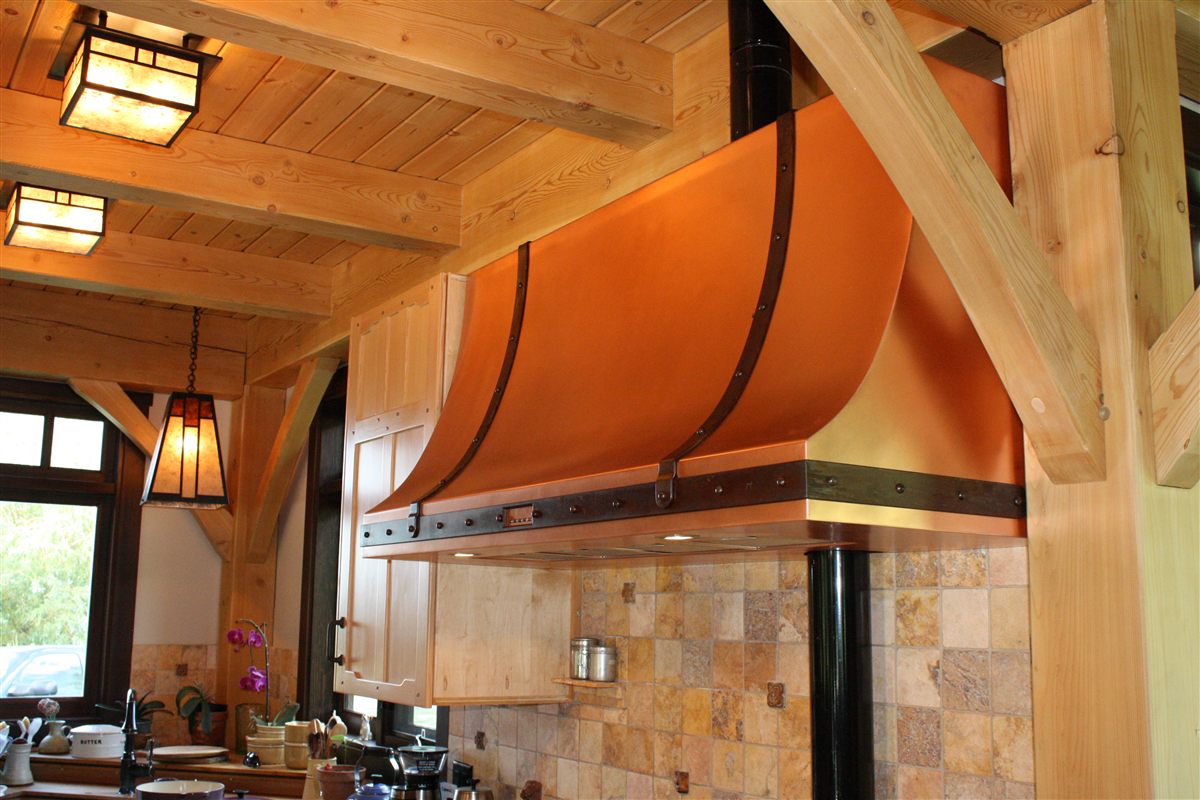 Curved copper range hood with riveted steel strapping in a timber-frame kitchen