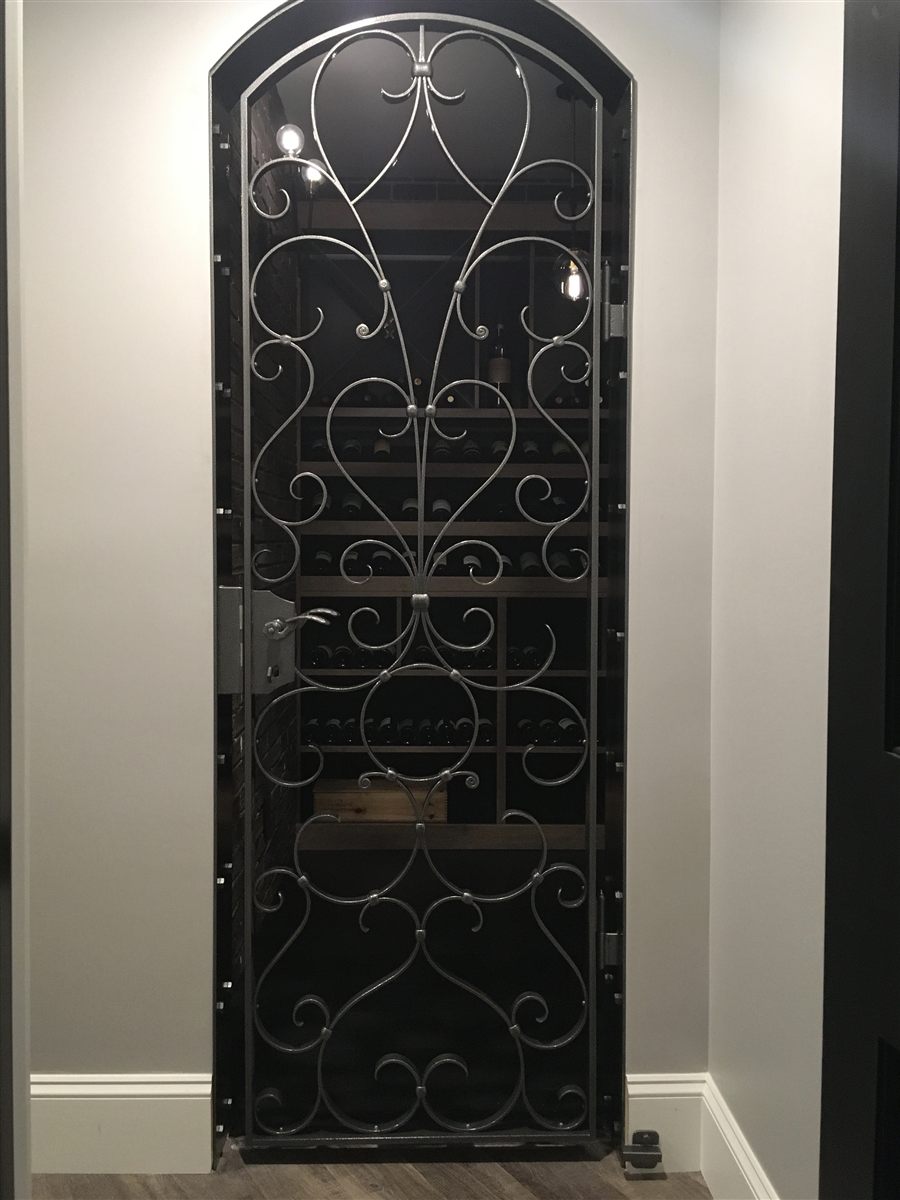 Hand-forged wine cellar gate installed, scrollwork over the wine racks